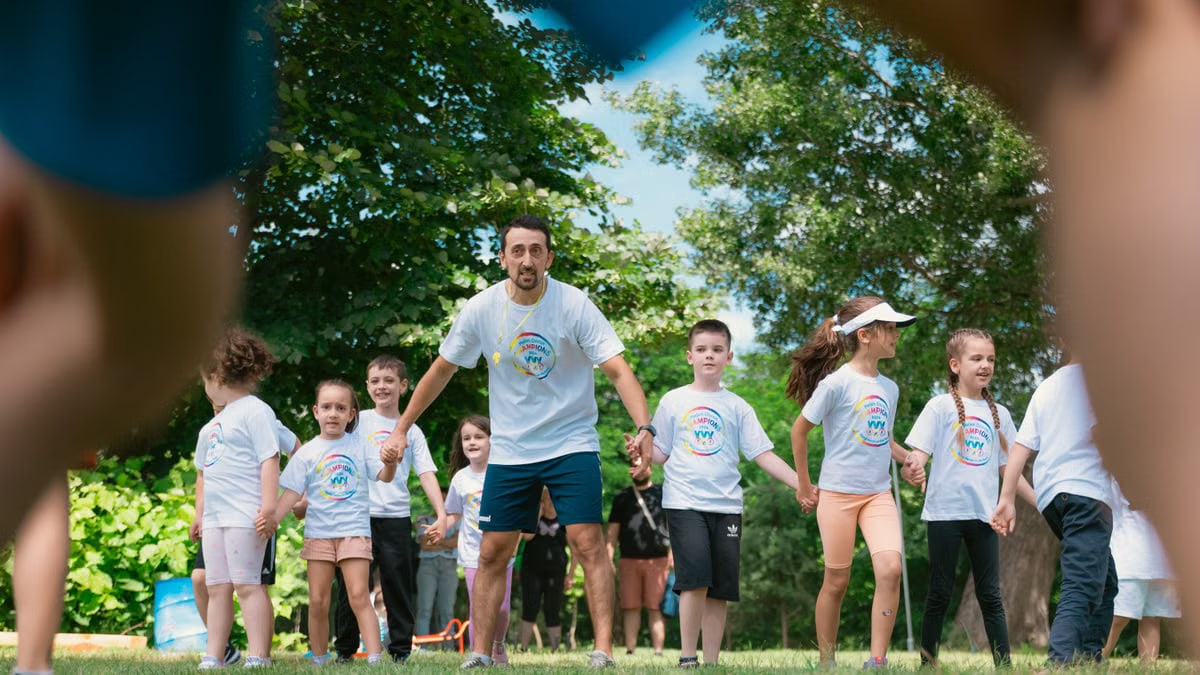 Children and an instructor playing together in a sunny park, holding hands and enjoying outdoor activities.