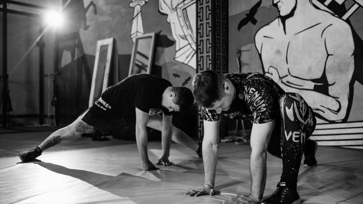 Two men stretching inside a gym, preparing for MMA training in a grayscale setting.